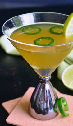 a drink in a martini glass garnished with limes and sliced jalapenos