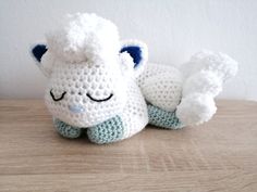 a crocheted white and blue stuffed animal laying on top of a wooden table