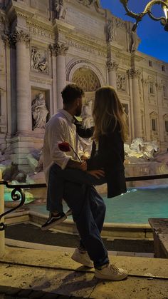 a man and woman sitting next to each other in front of a fountain at night