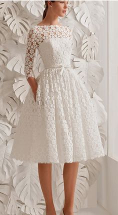 a woman in a white dress standing next to a wall with paper flowers on it