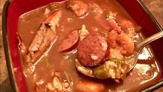 a red dish filled with meat and vegetables on top of a table next to a spoon