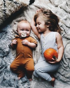 two children laying on a blanket with pumpkins in their hands and one holding a pacifier