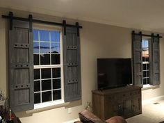 a flat screen tv sitting on top of a wooden stand in front of two windows