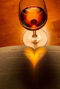 an open book next to a glass of wine on top of a wooden table with a lit candle