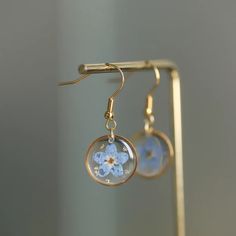 a pair of earrings with blue flowers hanging from it's earwires on a stand