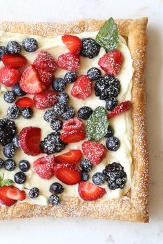 a pastry topped with berries and cream on top of a white counter next to a cup of coffee