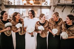 a group of women standing next to each other wearing fur coats and holding bouquets