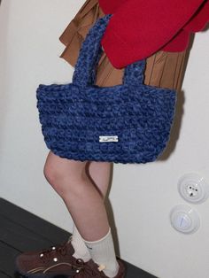 a woman carrying a blue crocheted purse on her feet and wearing brown shoes