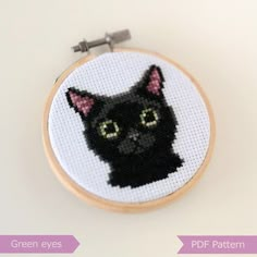 a cross stitch black cat with green eyes