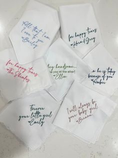 six embroidered napkins with different sayings are on the counter top, and one is white