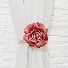 a pink flower sitting on the side of a white curtain in front of a brick wall