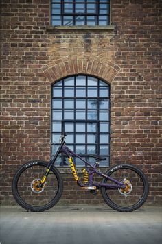 a purple and yellow bike parked in front of a brick wall next to a window