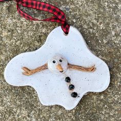 a snowman ornament hanging from a red ribbon on the ground next to some rocks