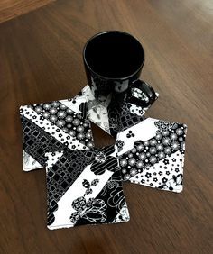 four coasters with black and white designs on them sitting on a wooden table next to a coffee cup