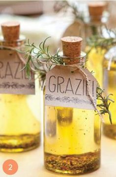 three small bottles filled with olive oil and rosemary sprigs on top of a table