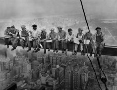 a group of men sitting on top of a tall building in the middle of a city