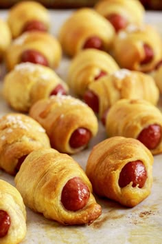 hotdogs wrapped in bread on a baking sheet with other pastries behind them