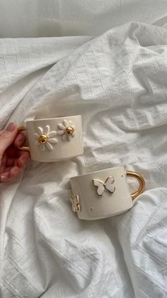 two white bracelets with gold bows on them sitting on a bed next to someone's hand