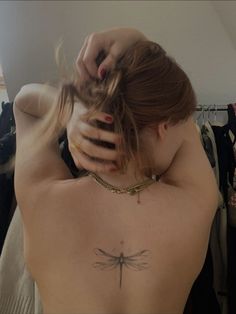 a woman with a dragonfly tattoo on her back is looking at the camera and holding her neck