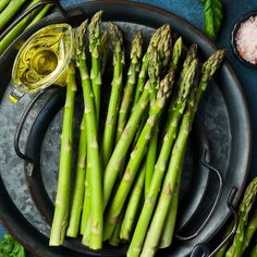 asparagus spears on a plate with salt and seasoning next to them, ready to be cooked