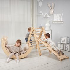 two children playing on wooden toys in a room with white walls and flooring,