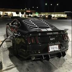 a black mustang parked in front of a gas station at night with its hood open