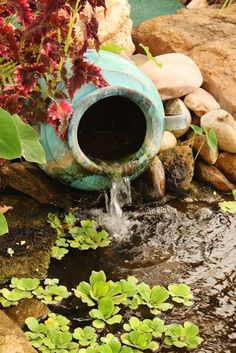 there is a water fountain in the middle of some plants and rocks with lily pads around it