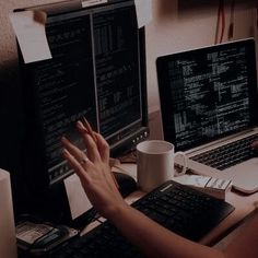 a woman sitting at a desk with two laptops and a coffee mug in front of her