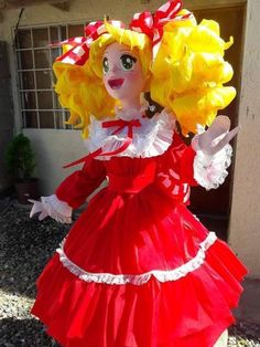 a doll dressed in red and yellow is standing next to a building with its arms out