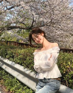 a young woman posing for a photo in front of some cherry trees with her hands on her hips