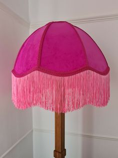 a pink table lamp with fringes on the base and a white wall behind it