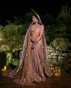 a woman in a pink lehenga standing on a wooden platform with candles around her