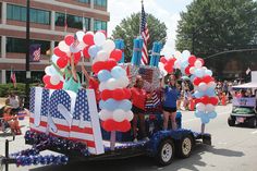 people are riding in the back of a truck with balloons and american flags on it