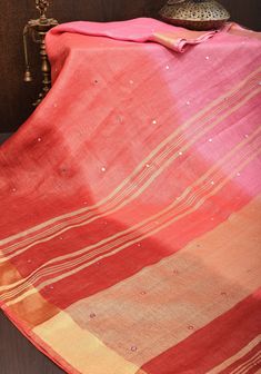 an orange and pink blanket sitting on top of a wooden table next to a lamp