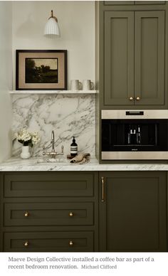 a kitchen with green cabinets and marble counter tops, along with a white vase filled with flowers