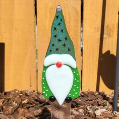 a green and white santa clause decoration sitting in front of a wooden fence