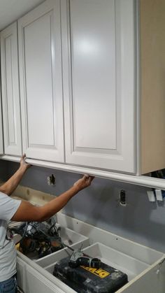 a woman working on cabinets in a kitchen with white cupboards and an electrical outlet