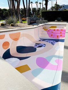 a skateboard park with colorful designs on the side and trees in the back ground