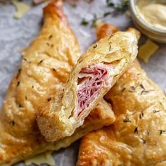 two pastries with meat and cheese are on wax paper next to a small bowl of sauce