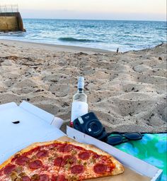 a pepperoni pizza sitting on top of a beach next to a bottle of water