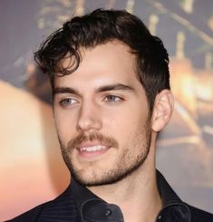 a close up of a person wearing a suit and tie with his hair pulled back