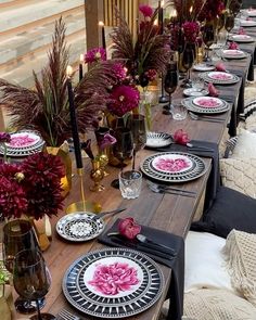 the table is set with black and white plates, pink flowers, candles and vases