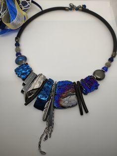 Beautiful modern style choker necklace with an ethnic touch. The necklace is made of large irregular flakes of agate and bone stone galvanized in blue and silver, hematite and glass beads. The central part of the necklace is made with rather large stones which make the necklace very eye-catching. This necklace is the fruit of my imagination, it is an artistic jewel created with various natural stones and crystals. The necklace is rigid but rests naturally on the neck, very comfortable to wear. The back is made with silicone cord. The necklace is very bright, 47cm long with an adjustable hook clasp. The necklace is in shades of blue, black, and silver which make it very elegant. It is a particular necklace, for those who love handmade pieces. The necklace is very elegant, very beautiful in Bohemian Choker For Party, Artistic Adjustable Choker Jewelry, Unique Adjustable Choker With Variations, Unique Adjustable Metal Crystal Necklaces, Unique Adjustable Choker With Unique Variations, One Of A Kind Adjustable Necklace For Parties, Adjustable Natural Stone Necklaces For Parties, Unique Natural Stone Necklaces For Parties, Artisan Necklace With Unique Variations For Party