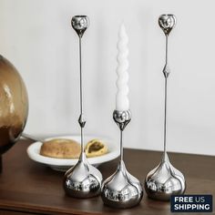 three silver candlesticks sitting on top of a wooden table next to a plate