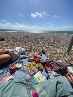 a man laying on top of a sandy beach next to the ocean with food and drinks