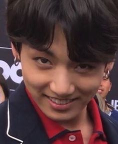 a close up of a person wearing a red shirt and black blazer smiling at the camera