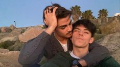 two young men sitting next to each other in front of some rocks and palm trees