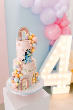 a pink cake with rainbows and balloons in the shape of a number four on top