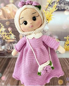 a crocheted doll with a pink dress and bonnet holding a flower in her hand