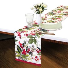 the table runner is decorated with red berries and green leaves, along with two glasses